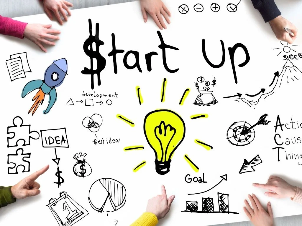 Eine Tischfläche mit Händen darauf die auf Skizzen zum Thema Startup deuten