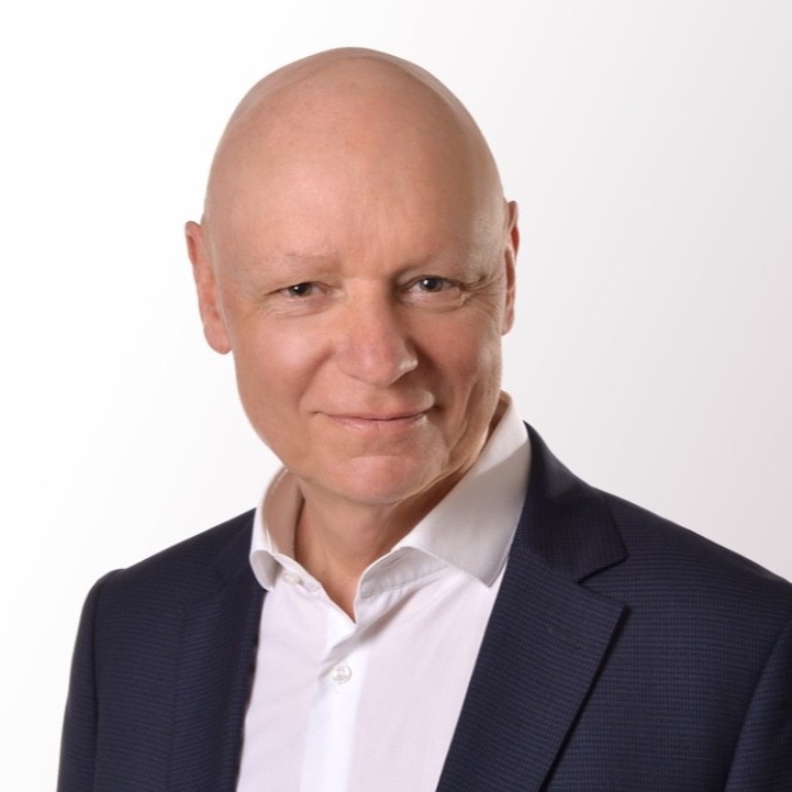 Das Bild zeigt den ZamStarten Trainer Dr. Detlef Pohl. Er hat eine Glatze und trägt ein weißes Hemd, darüber ein schwarzes Sakko. Er lächelt in die Kamera.