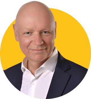 Das Bild zeigt den ZamStarten Trainer Dr. Detlef Pohl. Er hat eine Glatze und trägt ein weißes Hemd, darüber ein schwarzes Sakko. Er lächelt in die Kamera.