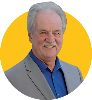 Das Bild zeigt den ZamStarten Trainer Norbert Alexy. Er hat graue, relativ kurze Haare und trägt einen grauen Sakko, darunter ein blaues Hemd. Er lächelt in die Kamera.