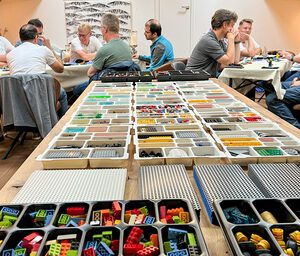 Zwei Gruppen von Männern sitzen an zwei Tischen und arbeiten mit dem Konzept LEGO® Serious Play®, also mithilfe von Lego-Bausteinen Klarheit im Denken und Planen zu schaffen. Im Vordergrund ist ein Tisch mit vielen verschiedenen Lego-Bausteinen zu sehen.