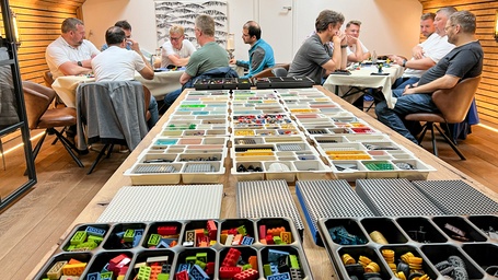 Zwei Gruppen von Männern sitzen an zwei Tischen und arbeiten mit dem Konzept LEGO® Serious Play®, also mithilfe von Lego-Bausteinen Klarheit im Denken und Planen zu schaffen. Im Vordergrund ist ein Tisch mit vielen verschiedenen Lego-Bausteinen zu sehen.